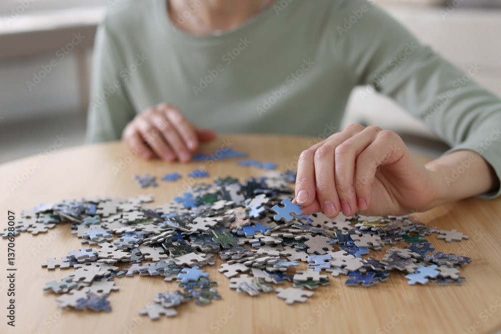 Woman solving puzzle at wooden table indoors, closeup Woman solving puzzle at wooden table indoors, closeup
