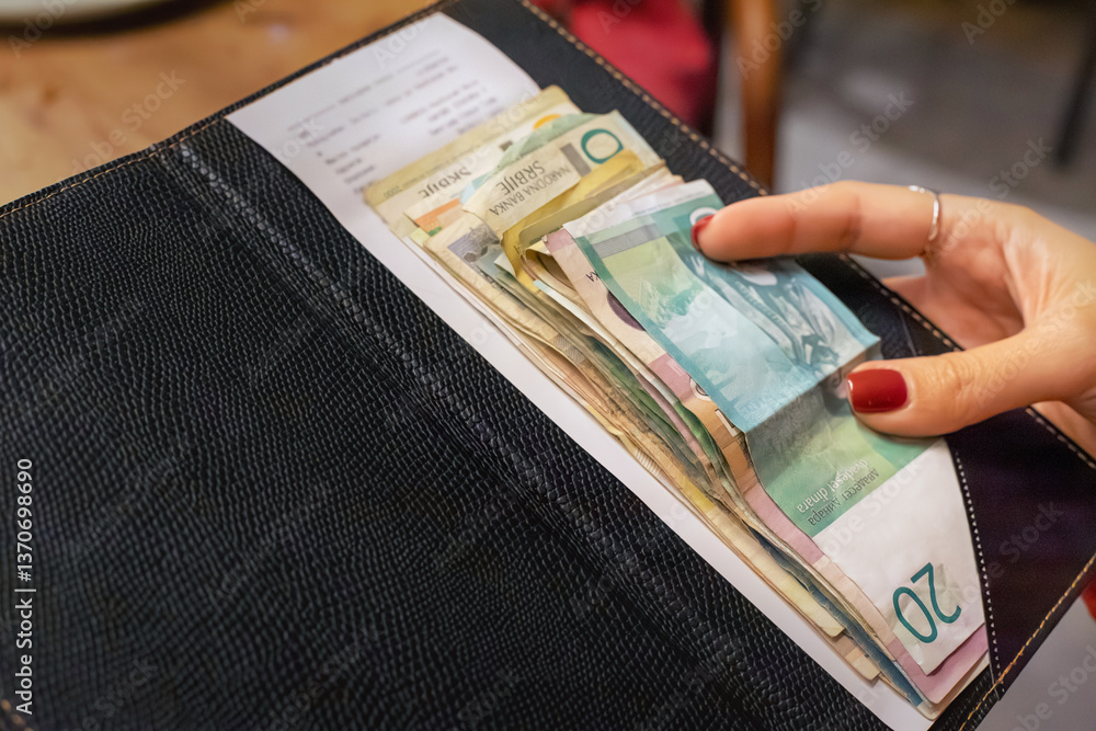 Stack of serbian dinar banknotes left on a restaurant bill inside a black bill folder placed on a wooden table, paying for the meal