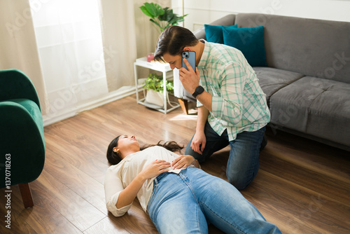 Man dialing 911, kneeling beside unconscious woman experiencing sudden medical emergency on ground