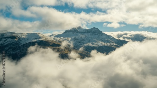 Snowy mountains peak through a blanket of fluffy white clouds and blue sky.