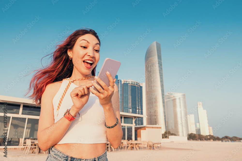 Young woman looking surprised at her phone screen while enjoying a sunny day on the beach in Abu Dhabi