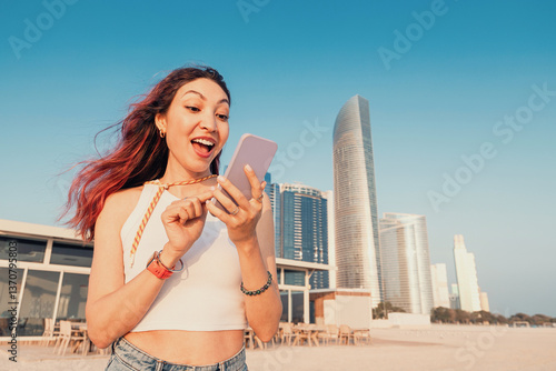 Obraz na płótnie Young woman looking surprised at her phone screen while enjoying a sunny day on the beach in Abu Dhabi w salonie