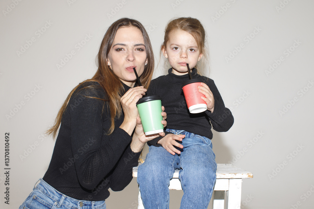 stylish mother with daughter, casual style, drinking milk shake on studio background