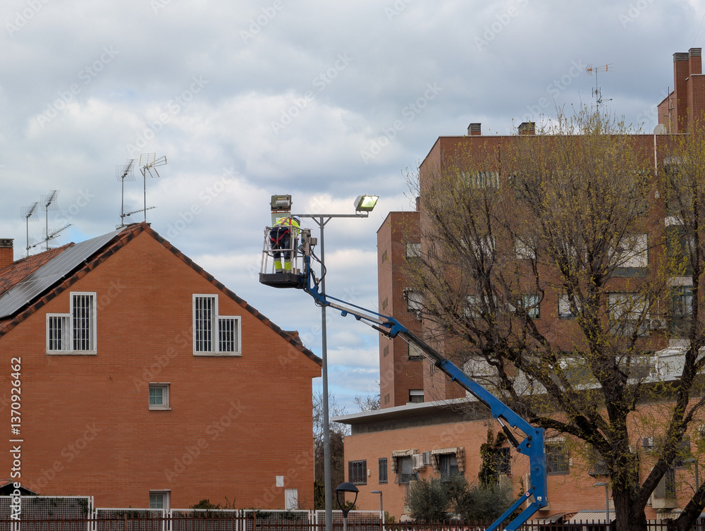 Worker repairs street light using lift in residential area durin