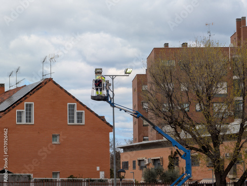 Worker repairs street light using lift in residential area durin