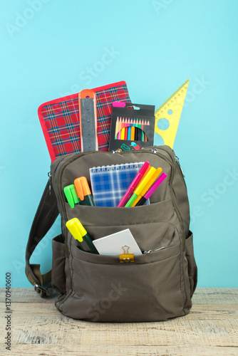 Backpack with different colorful stationery on table. Light blue background. Back to school.