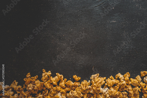 Obraz na płótnie Caramel popcorn scattered along the bottom edge on a dark rustic wooden background. Empty space above creates room for text or design w salonie