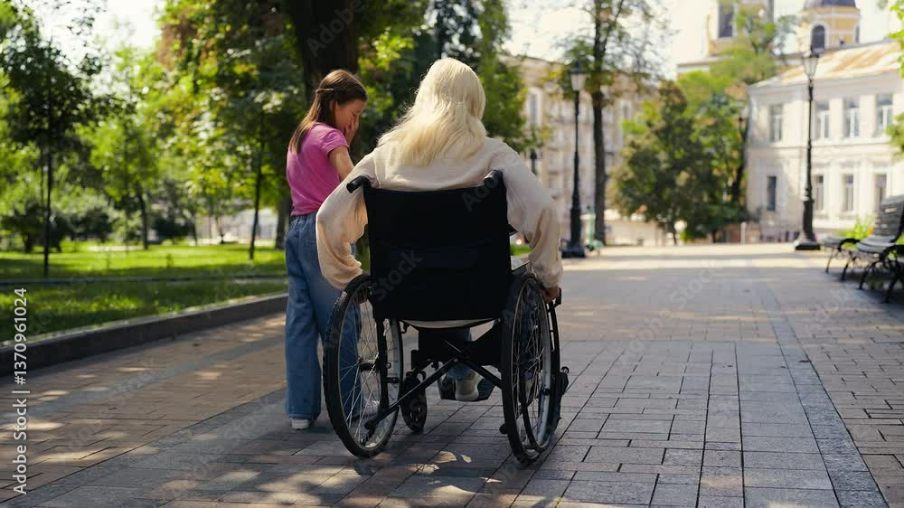 Young girl talks with mom wheelchair user during walk, part of rehab routine Young girl talks with mom wheelchair user during walk, part of rehab routine