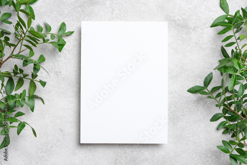 Vertical blank card mockup on grey concrete background, surrounded by vibrant green foliage. Invitations card or flyer with copy space