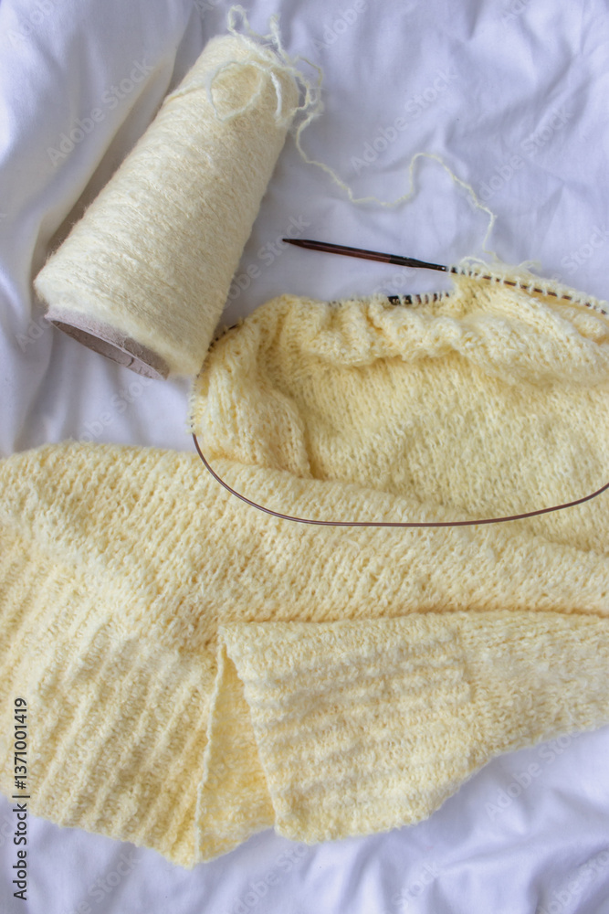 Yellow cotton knitting with knitting needles on white sheet. Soft yellow knitwear with circle needles. Knitting pattern background. Knitting lifestyle. Cozy hobby. Warm knitwear. Craft product concept