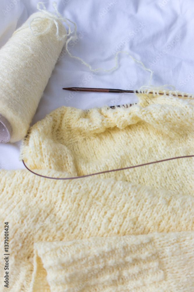 Yellow cotton knitting with knitting needles on white sheet. Soft yellow knitwear with circle needles. Knitting pattern background. Knitting lifestyle. Cozy hobby. Warm knitwear. Craft product concept