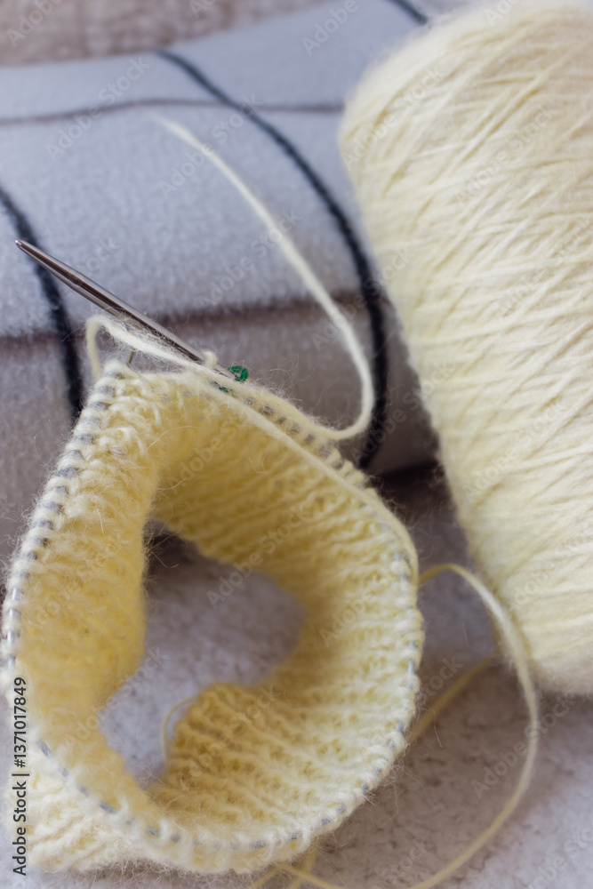 Yellow knitting with grey checkered plaid on sofa. Knitted fashion. Cotton knitting crochet with knitting needles and bobbin. Knitting hobby. Handmade knitted clothing. Cozy still life. Domestic life