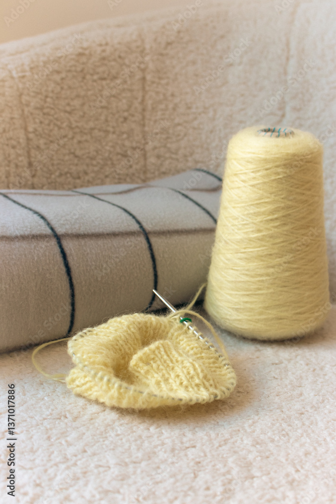 Yellow knitting with grey checkered plaid on sofa. Knitted fashion. Cotton knitting crochet with knitting needles and bobbin. Knitting hobby. Handmade knitted clothing. Cozy still life. Domestic life