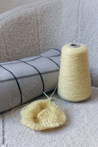 Obraz na płótnie Yellow knitting with grey checkered plaid on sofa. Knitted fashion. Cotton knitting crochet with knitting needles and bobbin. Knitting hobby. Handmade knitted clothing. Cozy still life. Domestic life w salonie