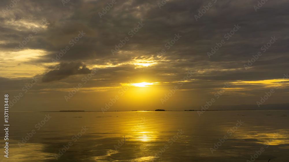 Naklejka premium Sunset over calm waters with reflections and dramatic clouds