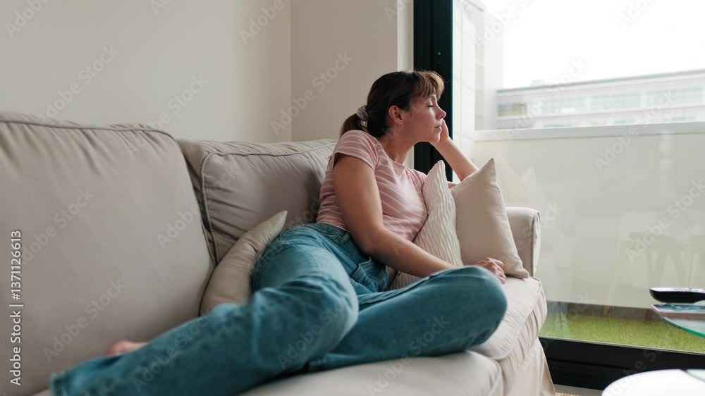 Thoughtful woman relaxing on the couch at home, resting, daydreaming, and looking out the window. Thoughtful woman relaxing on the couch at home, resting, daydreaming, and looking out the window.