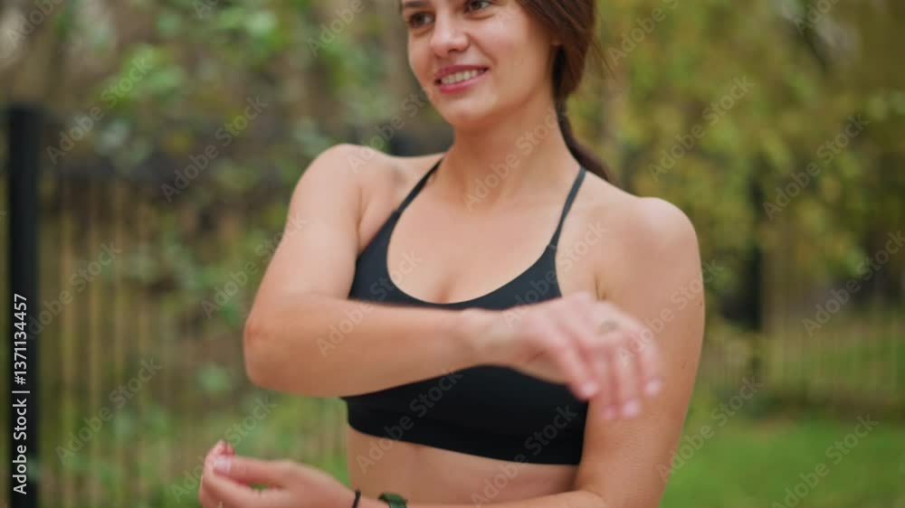 Portrait view of woman training outdoors with a smile on her face, wearing fitness wear, enjoying physical activity, with blurred background of trees and iron fence Portrait view of woman training outdoors with a smile on her face, wearing fitness wear, enjoying physical activity, with blurred background of trees and iron fence