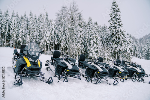 Fotografi Row of black snowmobiles stands in the snow on a mountain at a ski resort