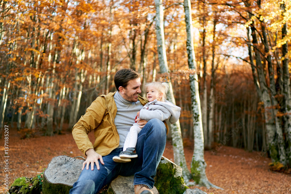 Fototapeta premium Smiling dad with a little girl on his knees sits on a stump 