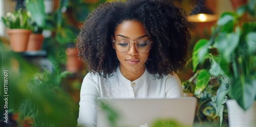 Young Woman Working on Laptop in a Vibrant Indoor Garden at a Cozy Cafe Durin...