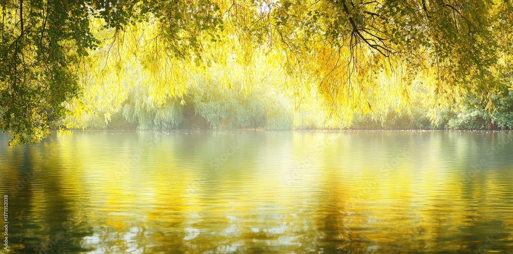 Fototapeta premium A serene landscape featuring a calm, reflective water body surrounded by lush, golden foliage under soft sunlight.