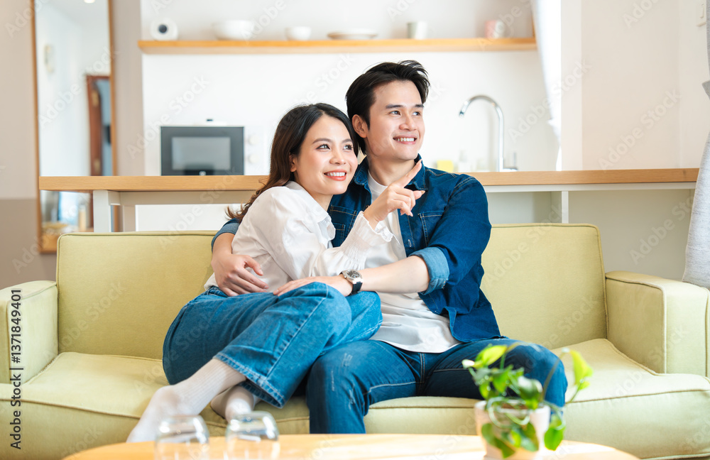 Happy couple relaxing together on the sofa pointing out into the distance enjoying free time Happy couple relaxing together on the sofa pointing out into the distance enjoying free time
