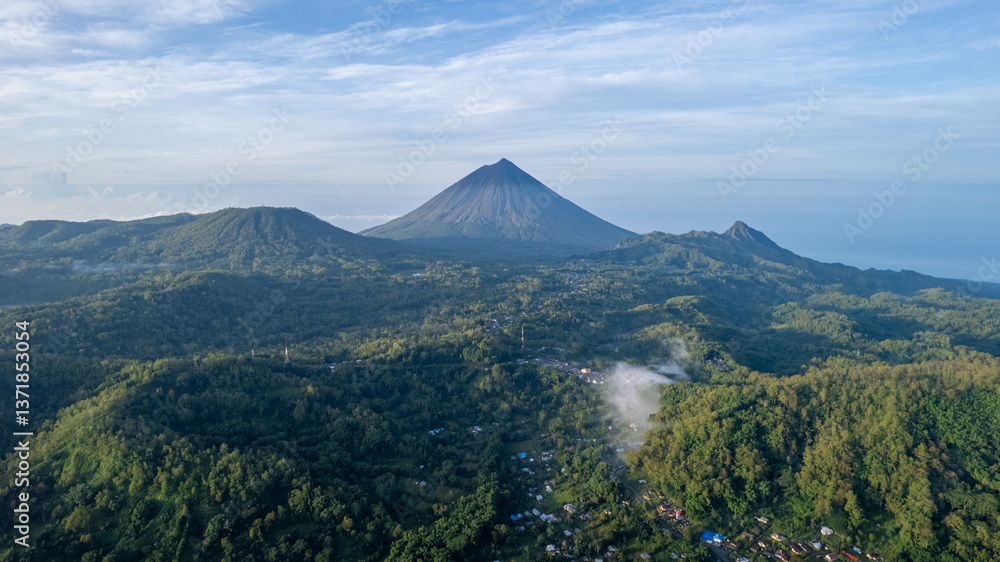 Fototapeta premium A breathtaking aerial view of Mount Inerie in the morning, surrounded by lush forests and thin mist. Small villages and houses are visible at the base, creating a serene and picturesque landscape.