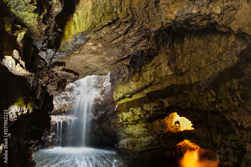Billede på lærred A waterfall inside Smoo cave illuminated by natural and artificial light
