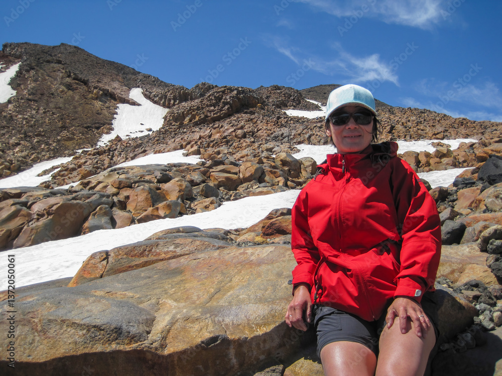 Woman taking a rest among ice covered rocks. Mt Ruapehu summit track. North Island. New Zealand.