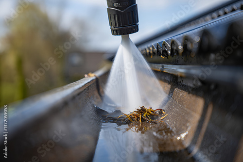 The process of cleaning spring rain gutters with a pressure washer, captured in a close, up photo to detail the task