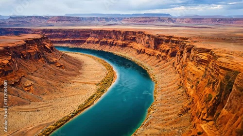 A sweeping view of a winding blue river cutting through red rock formations in a vast desert landscape under cloudy skies.