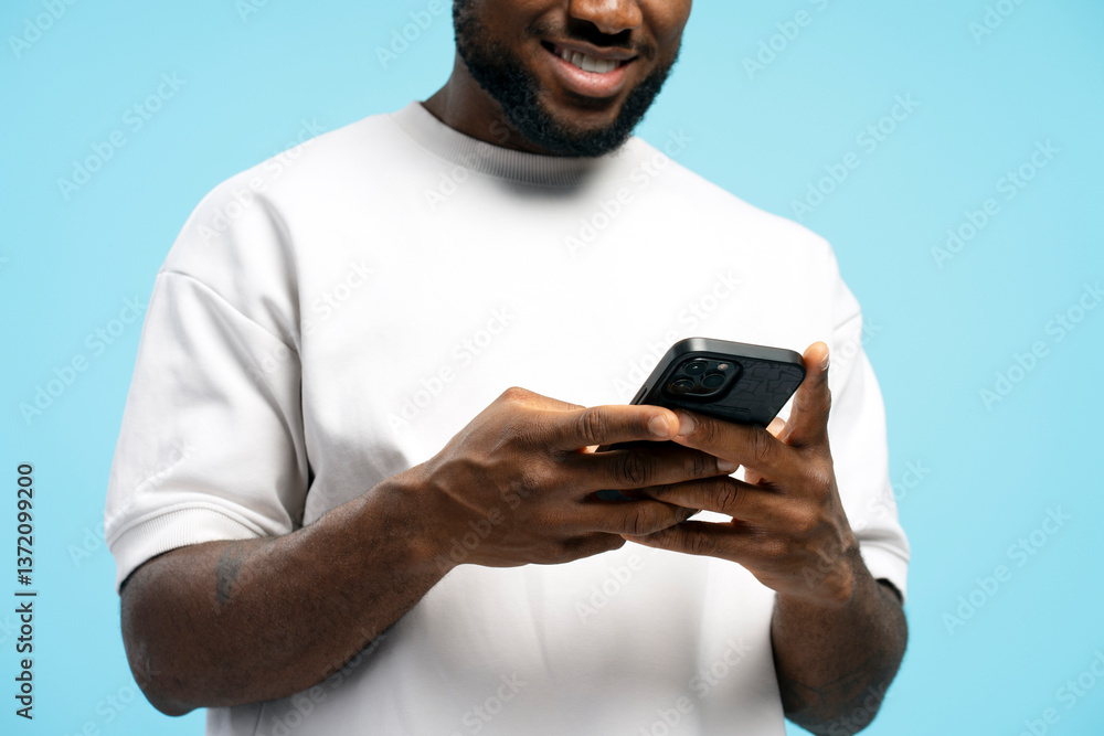 Smiling African American man holding mobile phone using mobile app on blue background Smiling African American man holding mobile phone using mobile app on blue background
