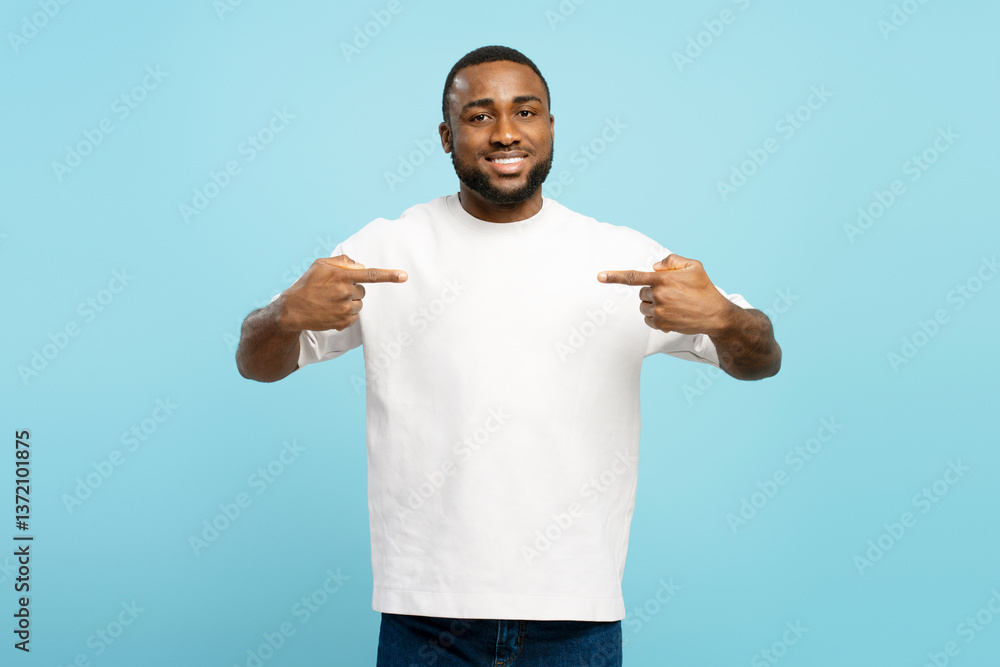 Smiling young African American man pointing at white t-shirt on blue background Smiling young African American man pointing at white t-shirt on blue background