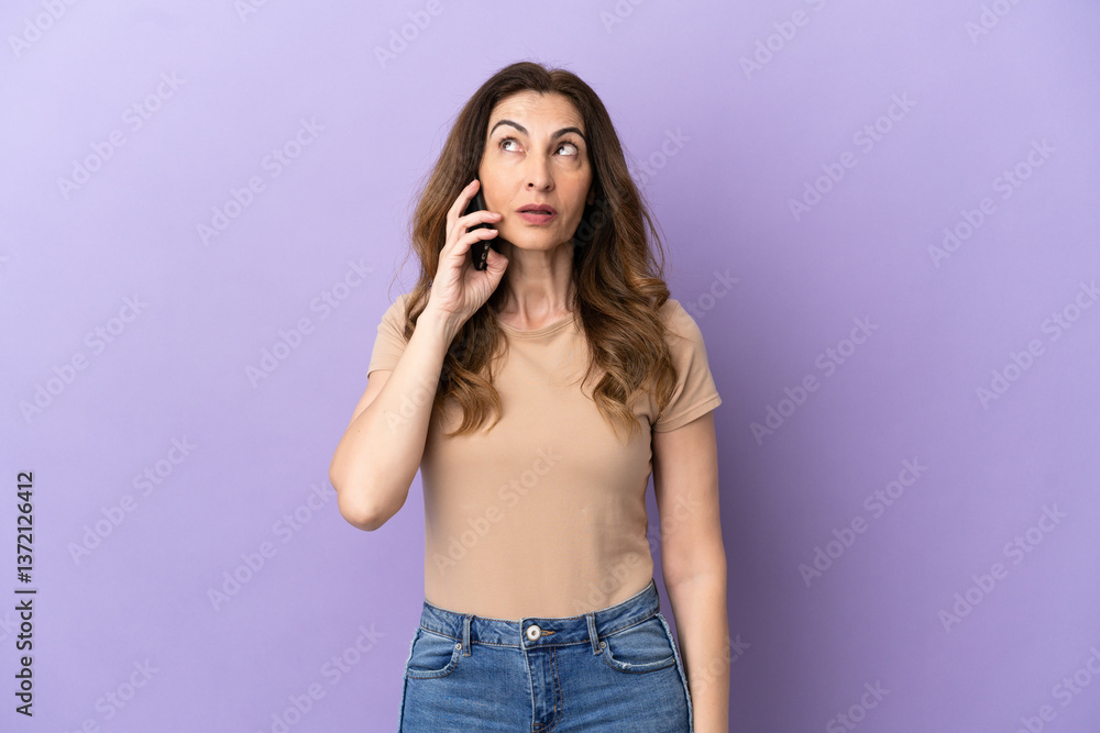 Middle aged caucasian woman using mobile phone isolated on purple background thinking an idea while looking up Middle aged caucasian woman using mobile phone isolated on purple background thinking an idea while looking up