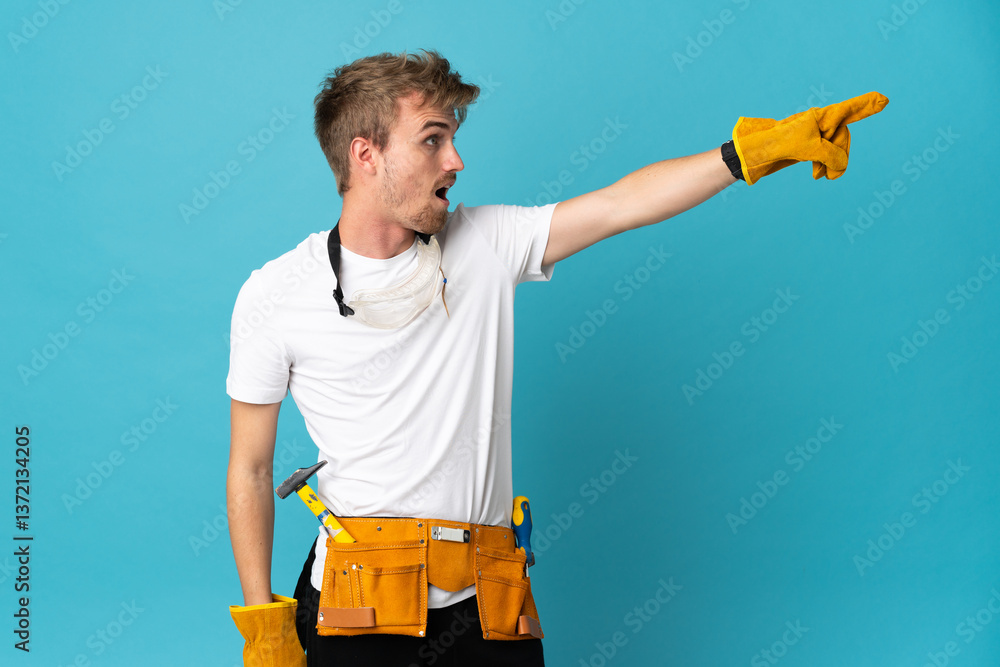 Young electrician man over isolated wall pointing away Young electrician man over isolated wall pointing away