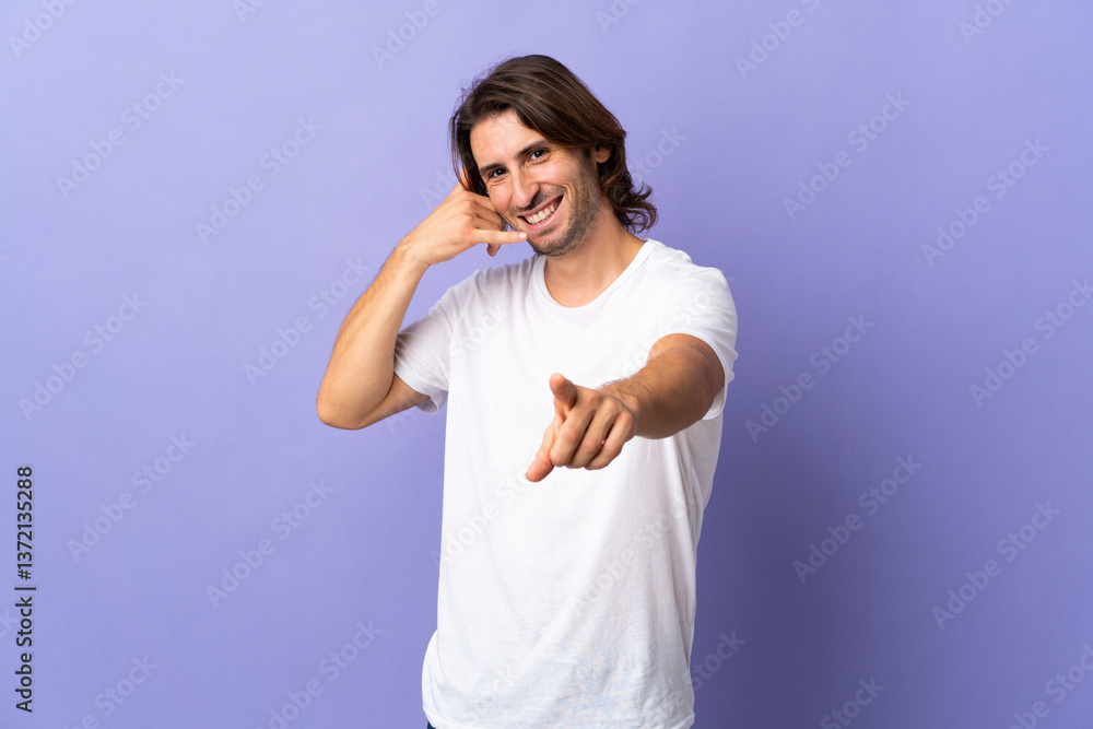 Naklejka premium Young handsome man isolated on purple background making phone gesture and pointing front