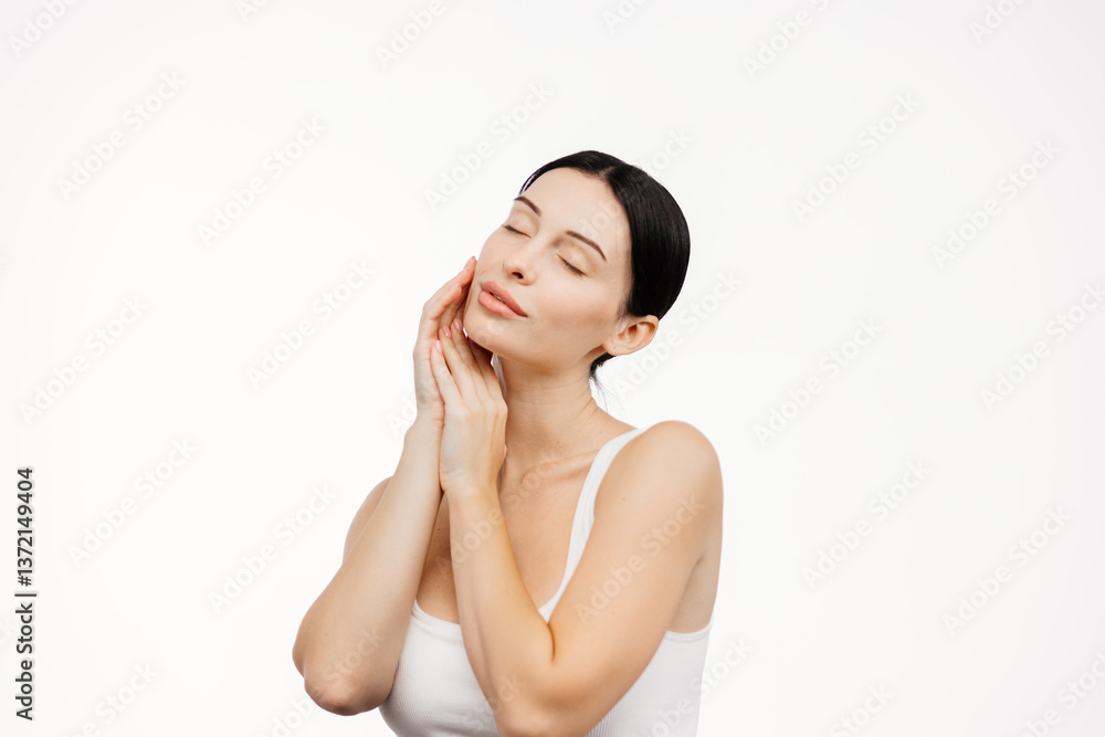 A young woman in a studio against a white background gently touches her flawless skin. Her facial expression conveys sensuality and harmony, emphasizing her attractiveness and well-groomed appearance. A young woman in a studio against a white background gently touches her flawless skin. Her facial expression conveys sensuality and harmony, emphasizing her attractiveness and well-groomed appearance.