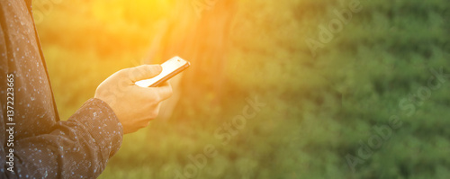 Obraz na płótnie A man holding a smartphone with a green-themed interface, illuminated by a soft lens flare. The blank copy space makes it ideal for advertisements, app promotions, or messaging concepts w salonie