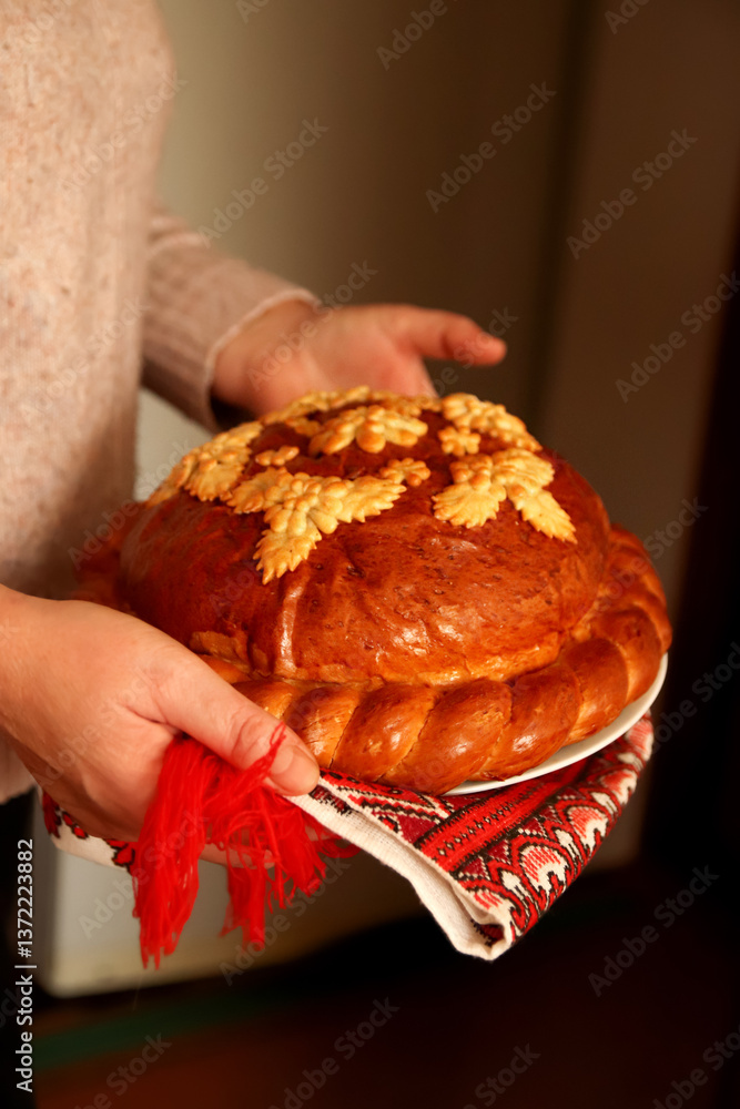 A traditional Ukrainian korovai held in hands, symbolizing celebration and hospitality. The beautifully decorated bread features intricate dough patterns, often with wheat motifs