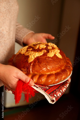A traditional Ukrainian korovai held in hands, symbolizing celebration and hospitality. The beautifully decorated bread features intricate dough patterns, often with wheat motifs