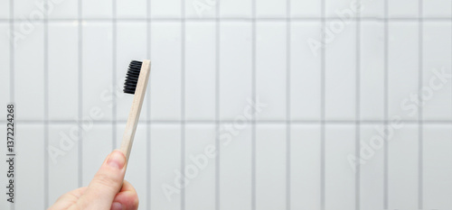 Obraz na płótnie A wooden eco-friendly toothbrush held in a hand against a clean white tile background, emphasizing themes of sustainability, oral hygiene, and natural living. Copy space w salonie