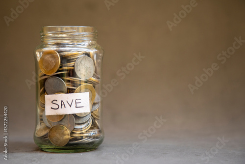 A glass jar labeled 'SAVE' is brimming with coins, signifying budgeting, frugality, and responsible financial practices. This image is ideal for themes of finance, economic planning, or thriftiness.