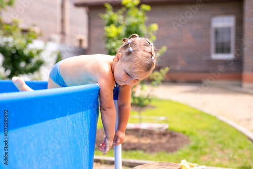 Little girl leaning over the edge of an inflatable pool on a sunny day in the backyard