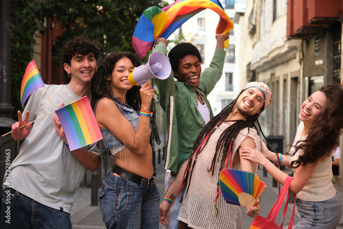 Group of happy multi ethnic friends celebrating gay pride holding rainbow flags and megaphone