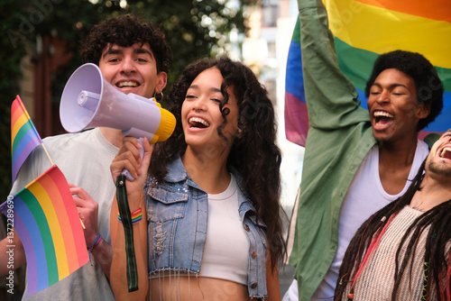 Group of young activists holding rainbow flags and shouting with megaphone at a lgbt pride parade