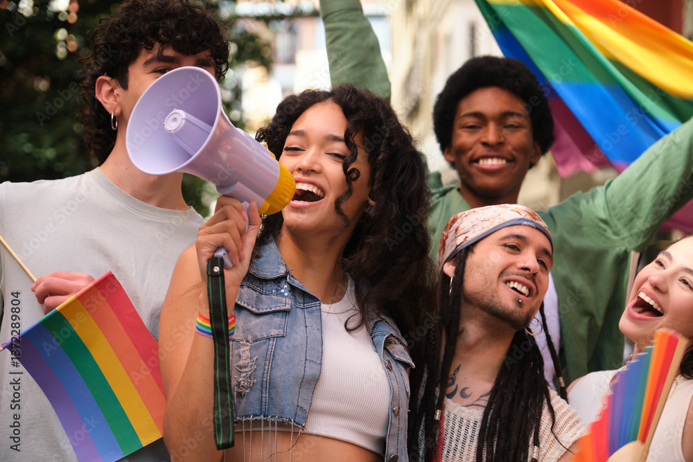 Young woman speaking with megaphone at LGBT pride parade with friends waving rainbow flags