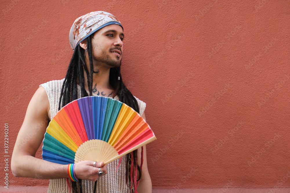 Portrait of a young man holding a rainbow hand fan and celebrating gay pride supporting LGBT community