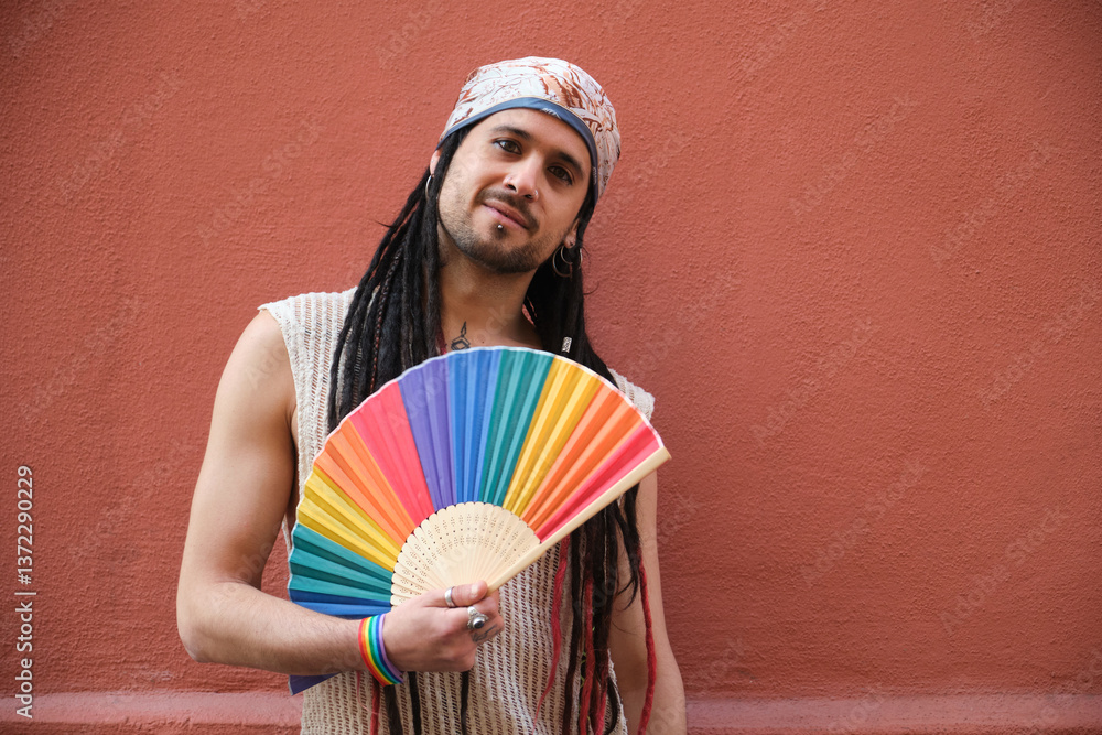 Portrait of a young artist with dreadlocks and bandana holding a rainbow hand fan celebrating gay pride supporting LGBT community