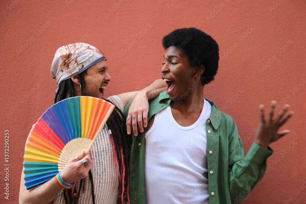 Two male friends are laughing and having fun together while celebrating LGBT pride, one of them is holding a rainbow fan