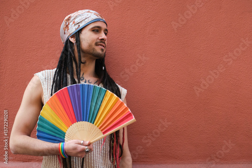 Obraz na płótnie Portrait of a young man holding a rainbow hand fan and celebrating gay pride supporting LGBT community w salonie